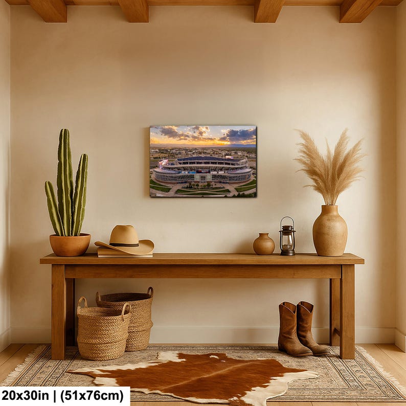 a wooden console table with a framed picture of a stadium, a potted cactus, a hat, a vase, and a pair of boots, all arranged on a rug.