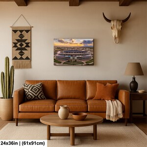 a cozy living room with a brown leather sofa, a wooden coffee table, and a large wall art piece depicting a stadium. The room is decorated with various items, including a hanging tapestry, a cow skull, and a potted plant. The overall atmosphere of the room is warm and inviting, with a harmonious blend of natural and man-made elements.