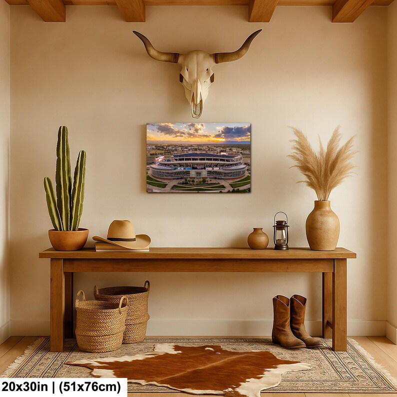 a wooden console table with a framed picture of a stadium, a potted cactus, a vase, a hat, and a pair of boots, all arranged on a cowhide rug.