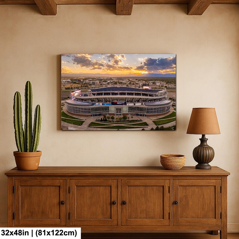 a large framed picture of a stadium hanging on a wall above a wooden cabinet.