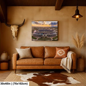 a living room with a brown leather sofa, a cowhide rug, and a large framed picture of a stadium on the wall.