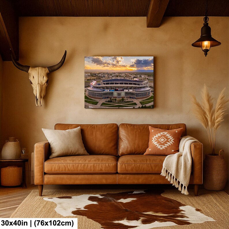 a living room with a brown leather sofa, a cowhide rug, and a large framed picture of a stadium on the wall.