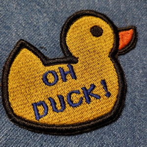 May include: Yellow rubber duck patch with black outline and blue embroidery that reads "OH DUCK!" on a blue denim background.