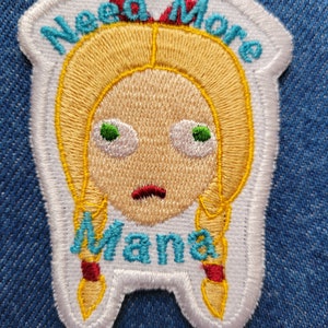 May include: White embroidered patch with a cartoon girl with blonde pigtails and the text "Need More Mama" in blue and red.