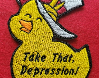 May include: Yellow embroidered patch of a cartoon duck wearing a white top hat with a red flower and the text "Take That, Depression!"