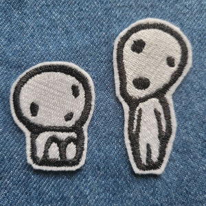 Peut inclure: Deux patchs thermocollants brodés blancs sur un fond en jean bleu. Les patchs représentent des personnages de dessins animés avec des contours noirs. Un personnage est une petite figure ronde assise avec une grosse tête et de petits membres. L'autre personnage est une grande figure mince avec une grosse tête et de longs bras et jambes.