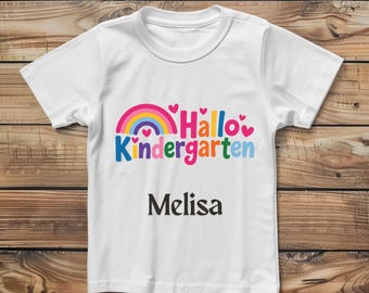 May include: White t-shirt with a colorful rainbow and the words "Hallo Kindergarten" in blue, pink, and yellow. Below the text is the name "Melisa" in black. The shirt is made of a soft material.