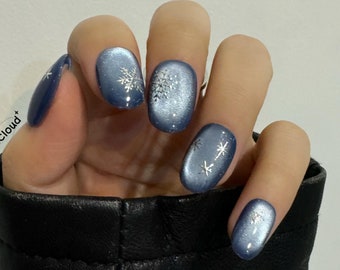 May include: Close-up of a hand with five fingernails painted a light blue color with silver snowflake designs.