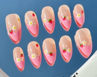 May include: Ten pink and white false nails with a strawberry and flower design. The nails are arranged in two rows on a blue surface.