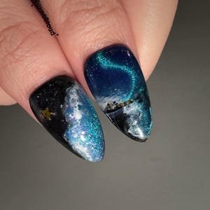 May include: Close-up of two fingernails with a celestial design. One nail is black with a gold star and white and blue glitter. The other nail features a dark blue sky with a shimmering green aurora borealis and a landscape.