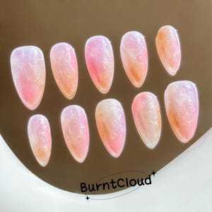 Op de afbeelding: Tien iriserende roze en witte kunstnagels met een textuur. De nagels zijn amandelvormig en hebben een verloop effect.