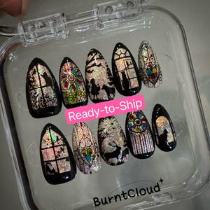May include: A set of ten black press-on nails with a stained glass design. Each nail features a different design, including cats, deer, and floral patterns. The nails are in a clear plastic case. The text "Ready-to-Ship" is visible.