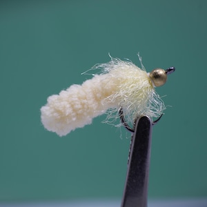 May include: A white and yellow fly fishing lure with a gold bead.