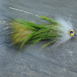 May include: A handmade fishing fly with a curved hook. The fly features a white, green, and brown feathered body with a gold-colored eye. The fly is designed to mimic an insect and attract fish.