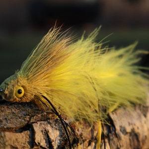 May include: A yellow and brown fly fishing lure with a large eye and a long tail of feathers.