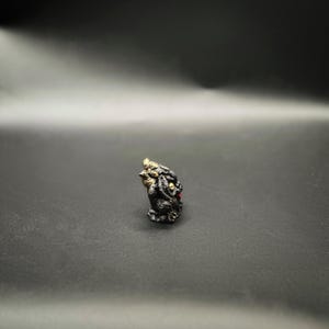 Pu&ograve; includere: Piccola e dettagliata statuetta di una creatura mitica, forse un drago o un gargoyle. La scultura &egrave; principalmente nera con accenti dorati e piccoli dettagli rossi. La figura &egrave; in posizione eretta, con trame e dettagli intricati.