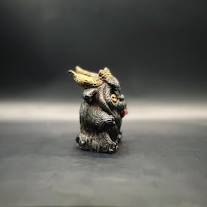 Left side view of Krampus, he has a black coat with brown over wash, gold horns, button eyes and speckles of gold on his paws with a cherry red tongue!