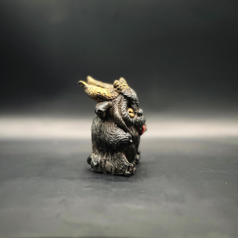 Left side view of Krampus, he has a black coat with brown over wash, gold horns, button eyes and speckles of gold on his paws with a cherry red tongue!