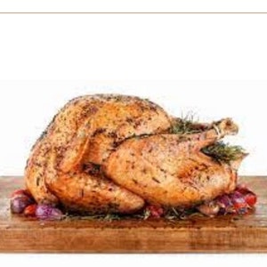 May include: A roasted turkey on a wooden cutting board with red and purple onions and herbs.