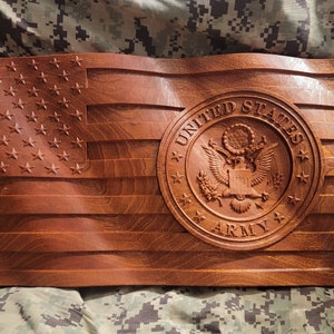 以下が含まれることがあります： アメリカ軍の刻まれた紋章がついた木製のアメリカ国旗。旗は濃い赤褐色で、波打つような質感です。