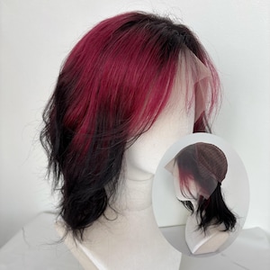 Peut inclure: Perruque courte et superposée avec un mélange de couleurs. Le dessus est rouge vif, se fondant en noir aux racines et aux pointes. La perruque est coiffée avec une raie sur le côté et une ligne de cheveux naturelle.
