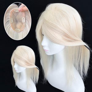 May include: A platinum blonde hair topper with a monofilament base and four metal pressure-sensitive clips attached to the underside. The hair is straight and shoulder-length, displayed on a white mannequin head with a side-swept fringe.
