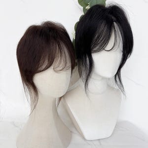 以下が含まれることがあります： マネキンの頭部に装着された2つのヘアトッパー。1つはダークブラウン、もう1つはブラックです。どちらも顔を縁取るような軽やかなレイヤー入りの前髪が特徴で、サイドには長めの毛束が自然に馴染むようにデザインされています。