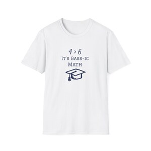 May include: White t-shirt featuring the navy blue text "4 > 6 IT'S BASS-IC MATH" and a navy blue graduation cap graphic. The t-shirt has a crew neck design.