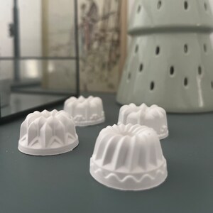 Könnte beinhalten: Vier weiße Keramik-Kuchenformen mit geriffeltem Design. Die Formen sind auf einer grauen Oberfläche angeordnet.