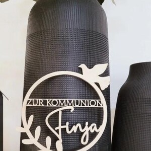 May include: Wooden cake topper with a circle and a dove, the text "Zur Kommunion" and the name "Finja".