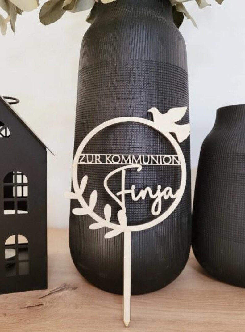 May include: Wooden cake topper with a circle and a dove, the text "Zur Kommunion" and the name "Finja".