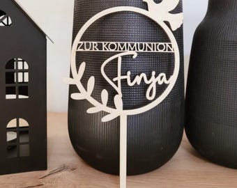 Pode incluir: Topo de bolo de madeira com um círculo, uma pomba e o texto "Zur Kommunion Finja".