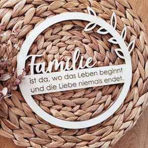 Puede incluir: Un letrero de madera con un círculo y una corona de hojas alrededor de la palabra "Familie". El letrero dice "is da, wo das Leben beginnt und die Liebe niemals endet."
