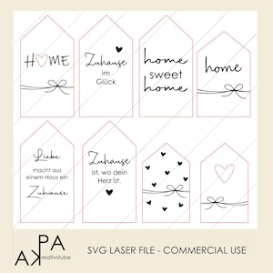 Könnte beinhalten: Acht weiße hausförmige Anhänger mit schwarzem Text und dekorativen Schleifen. Die Anhänger enthalten Sätze wie "HOME", "home sweet home" und deutsche Sätze. Kleine Herzen sind ebenfalls in den Designs enthalten.