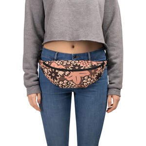 Peut inclure: Une banane à motif floral brun et rose avec une boucle noire réglable. La banane est portée autour de la taille d'une personne portant un jean bleu.
