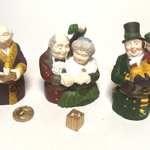May include: Set of four ceramic Christmas figurines. The figurines depict a man in a brown robe holding a candle, a couple holding hands, a man in a green coat holding a child, and a gold coin.
