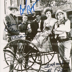 May include: Black and white photo of five actors from a Western television show. The actors are standing in front of a building and a horse-drawn carriage. The actors are all smiling and looking at the camera. The photo is signed by all five actors.