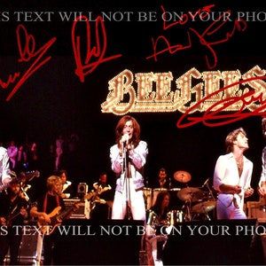 May include: A black and white photo of the Bee Gees band performing on stage. The band members are wearing white shirts and pants. The band's name is written in large, illuminated letters above the stage. The photo is signed by the band members.