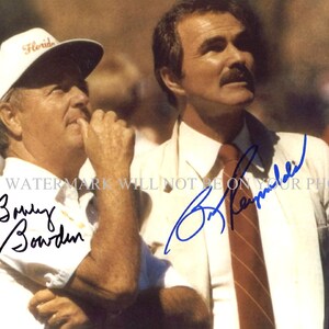 May include: A black and white photo of two men, one wearing a white hat with the word "Florida" on it, and the other wearing a white shirt and a red tie. Both men are smiling and looking up. The man in the white hat has a signature that says "Bobby Bowden" and the man in the white shirt has a signature that says "Bob Reynolds".