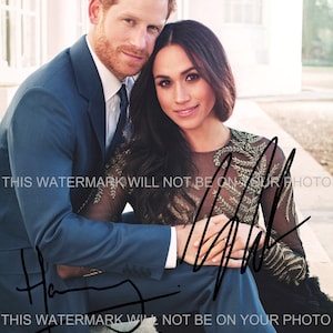 May include: A black and white photo of a couple sitting together. The man is wearing a blue suit and the woman is wearing a black dress with gold embroidery. The couple is smiling and looking at the camera.