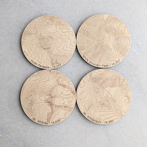 May include: Four wooden coasters with engraved maps of mountains. Each coaster features the name and elevation of a mountain: North Palisade - 14,249', White Mountain Peak - 14,252', Mt. Whitney - 14,505', and Mt. Williamson - 14,380'.