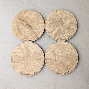 May include: Set of four wooden coasters featuring topographic maps of four mountains: Sundial Peak (10,320 ft), Mt. Olympus (9,028 ft), Mt. Superior (11,046 ft), and  Pfeifferhorn (11,331 ft).