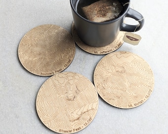May include: Four wooden coasters with laser-etched topographic maps of mountains. Each coaster features the name and elevation of a mountain: Boundary Peak - 13,146', Wheeler Peak - 13,085', Mt. Jefferson - 11,946', and Mt. Morlah - 12,072'.