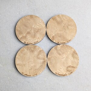 May include: Set of four wooden coasters featuring topographic maps of four mountains: Mt. Monroe, Mt. Adams, Mt. Washington, and Mt. Jefferson. Each coaster includes the mountain's name and elevation in feet.