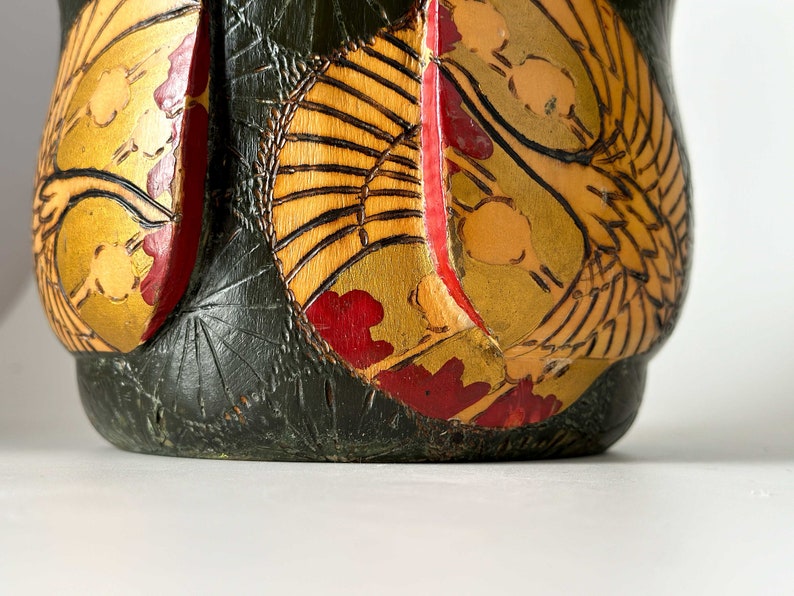 May include: A dark green wooden vase with a gold and red floral design. The vase has a round shape and a wide mouth.