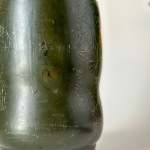May include: A dark green ceramic vase with a floral pattern and the text "M-N-3" written on the side.