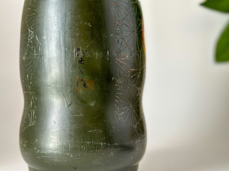 May include: A dark green ceramic vase with a floral pattern and the text "M-N-3" written on the side.