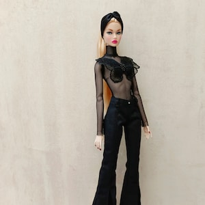 May include: A fashion doll wearing a black mesh top with a high collar and a decorative bodice, paired with black flared pants. The doll has blonde hair, a black headband, and is posed against a neutral background.