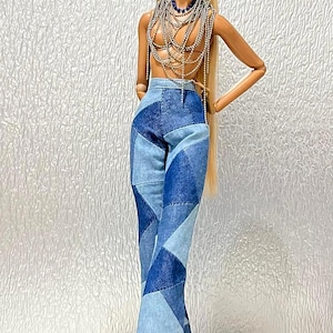 May include: A fashion doll with long blonde hair wearing high-waisted, flared denim pants featuring a patchwork design of various blue shades. The doll is adorned with multiple layered silver-toned chain necklaces that drape over the torso.