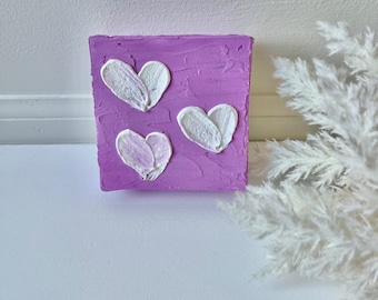 May include: A small purple canvas painting with three white painted hearts.